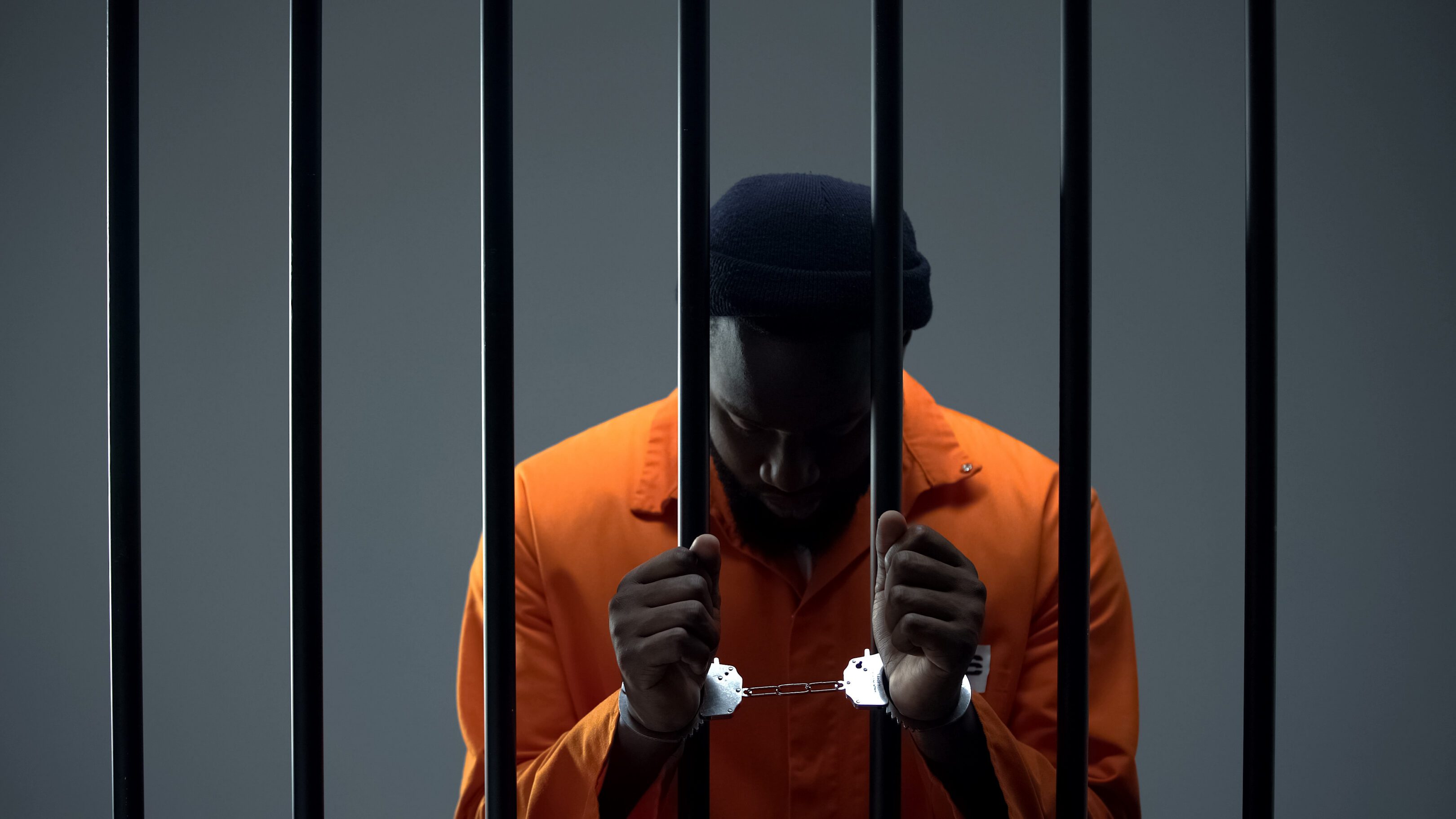 Upset afro-american criminal in handcuffs holding prison bars, regretting past