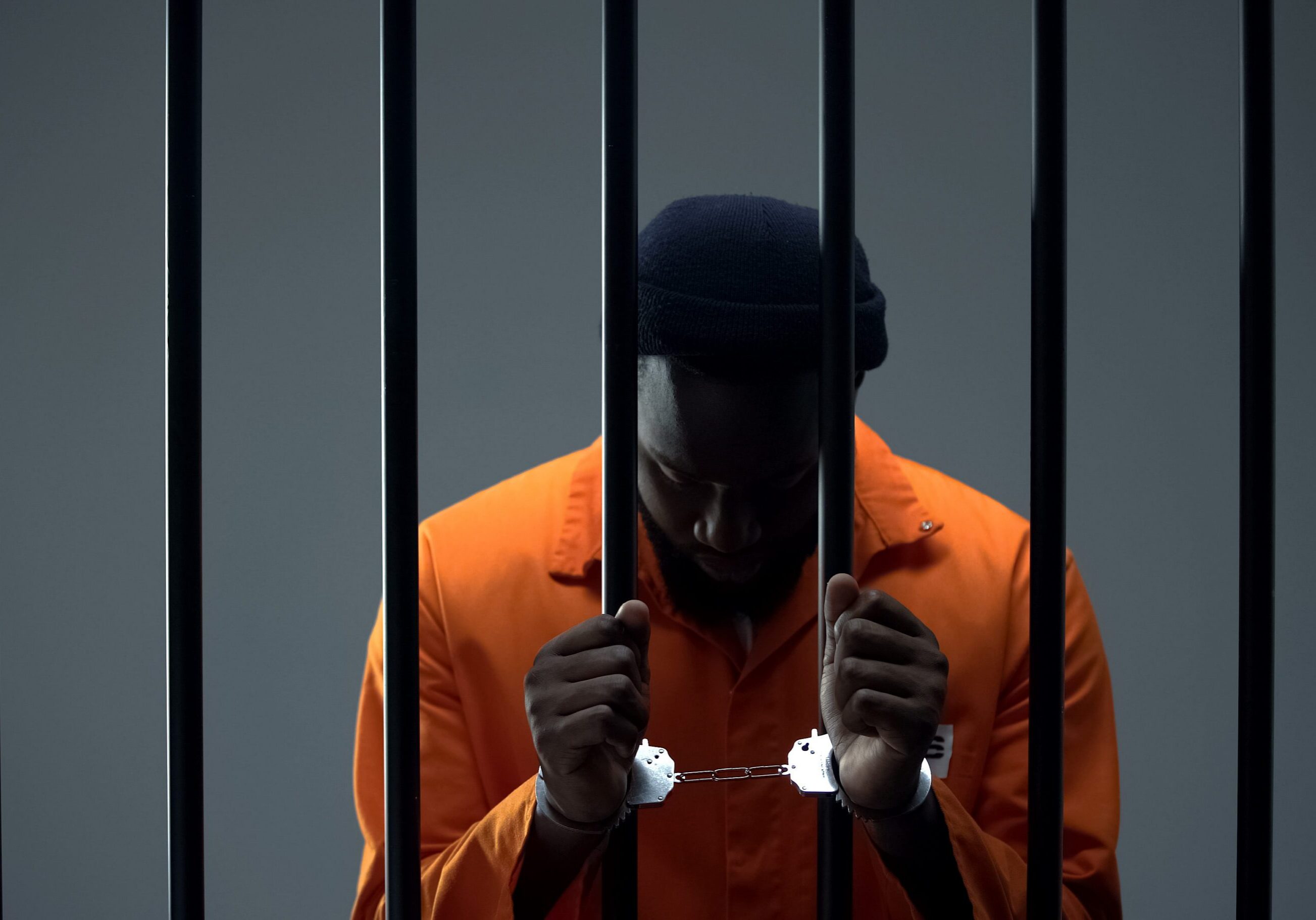 Upset afro-american criminal in handcuffs holding prison bars, regretting past